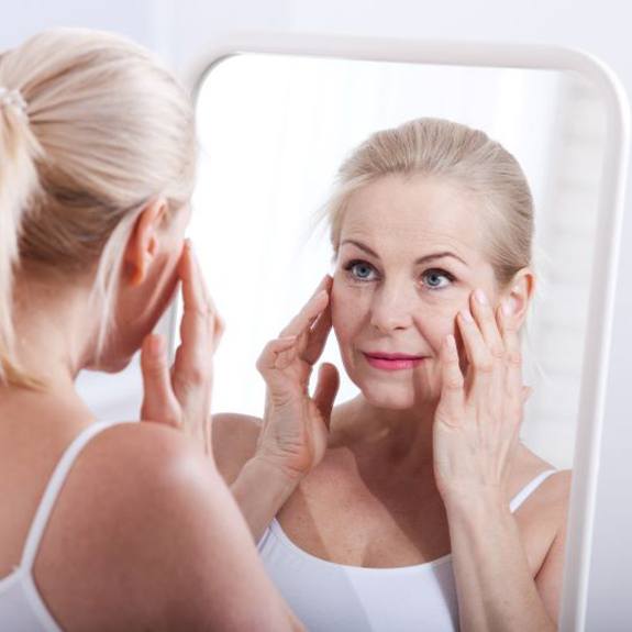 Woman looking in mirror, concerned about signs of aging